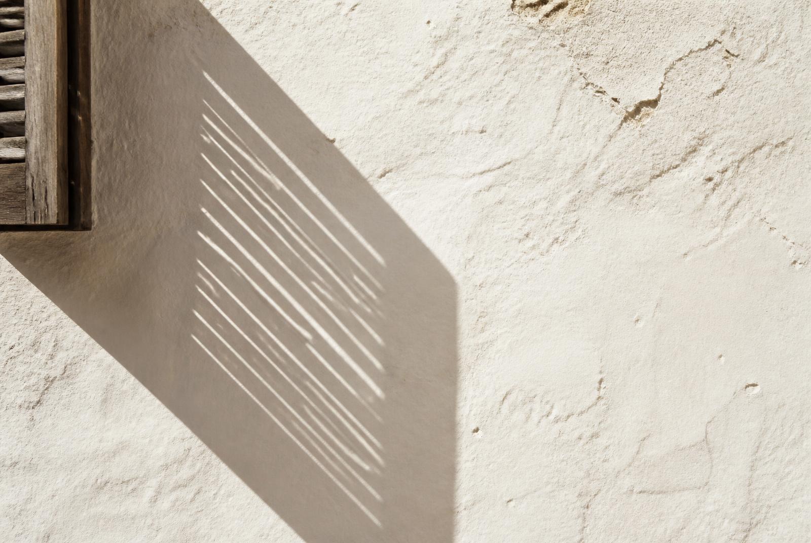 Sombra geométrica de una persiana de lamas de madera proyectada sobre un muro encalado
